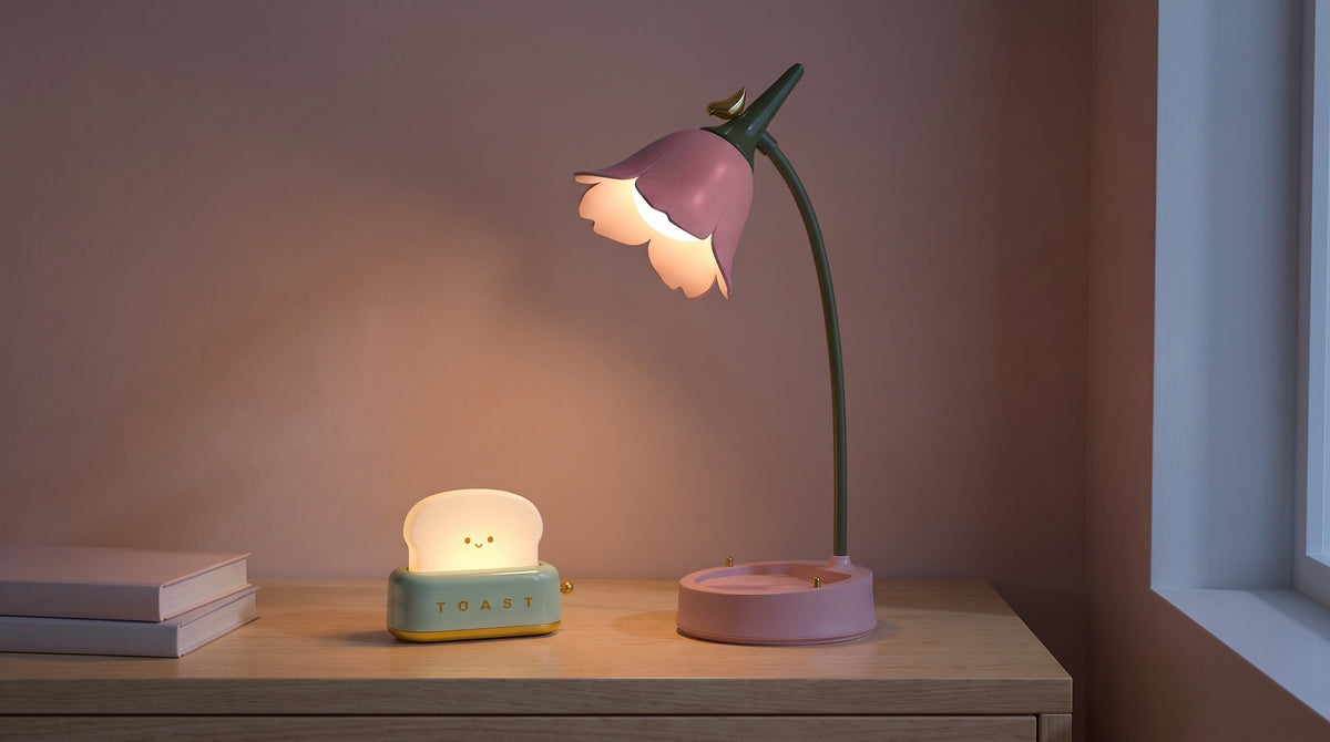 A pink flower desk lamp and a toaster night light glowing on a wooden nightstand at dusk