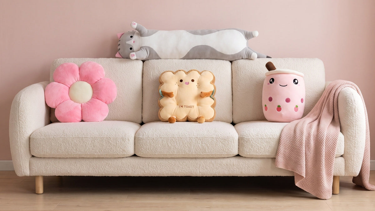 A flower pillow, a toast cushion and a boba plush pillow on a cream sofa, with a long cat plush pillow lying along the back