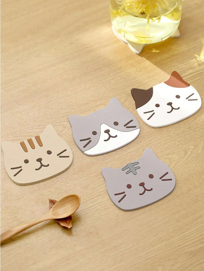 Tabby, grey-and-white, calico and grey cat coasters on a wooden table beside a glass and a wooden spoon