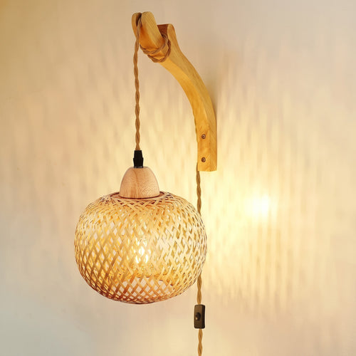 Bamboo Globe Plug-In Wall Sconce on a curved wood arm, lit on a plain wall, with its jute-wrapped cord and inline switch