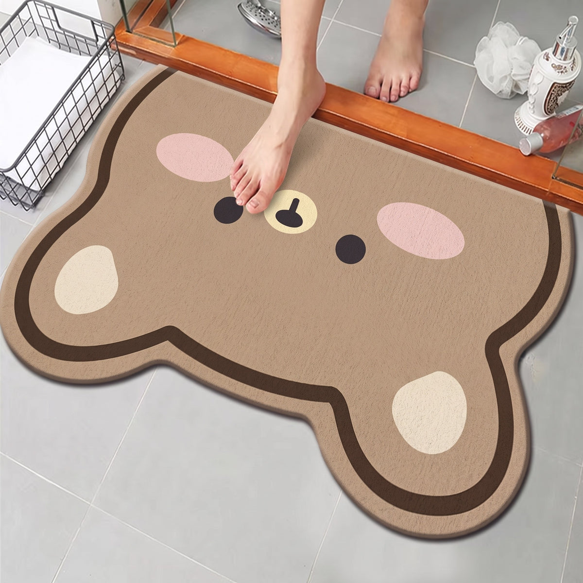 Bear Bath Mat, Big-Eared Bear design: a tan bear face with big round ears and pink cheeks, on a tiled bathroom floor at a shower door
