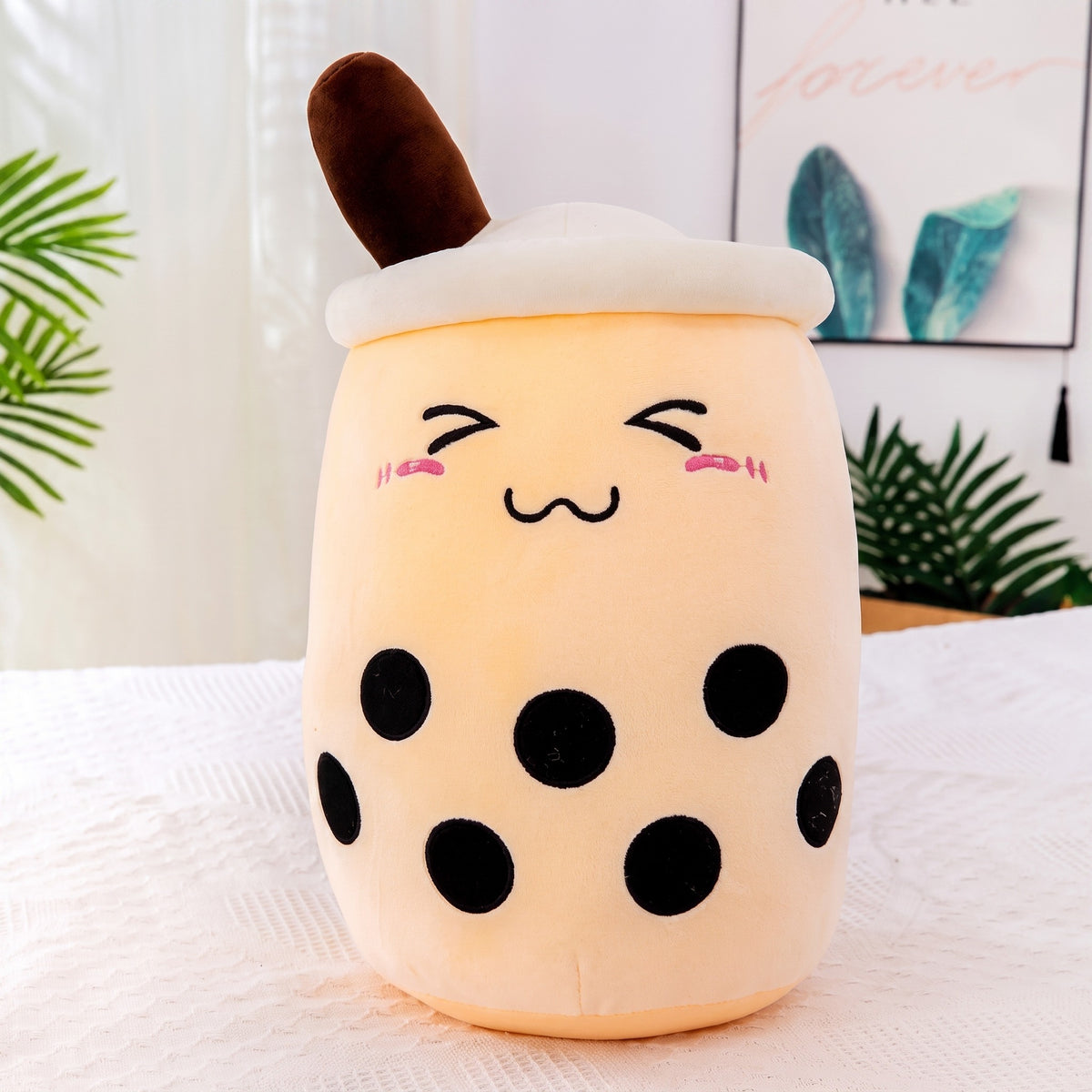 Boba Plush Pillow in beige, closed happy eyes and blushing cheeks, a plush bubble-tea cup with a cream lid, straw and pearls