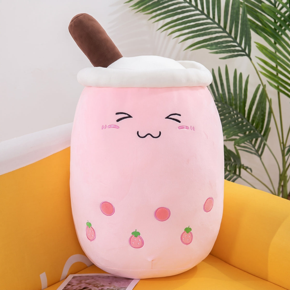 Boba Plush Pillow in pink with strawberry prints, closed happy eyes and blushing cheeks, a plush bubble-tea cup with a cream lid, straw and pearls