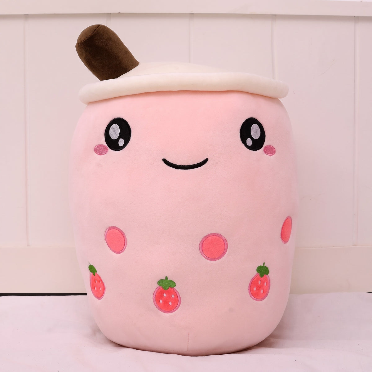 Boba Plush Pillow in pink with strawberry prints, wide open eyes and blushing cheeks, a plush bubble-tea cup with a cream lid, straw and pearls