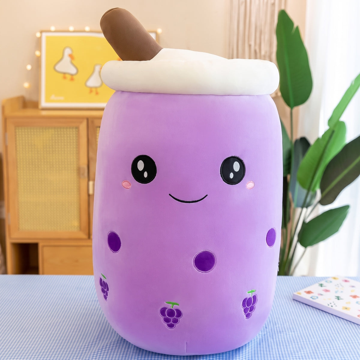 Boba Plush Pillow in purple with grape prints, wide open eyes and blushing cheeks, a plush bubble-tea cup with a cream lid, straw and pearls