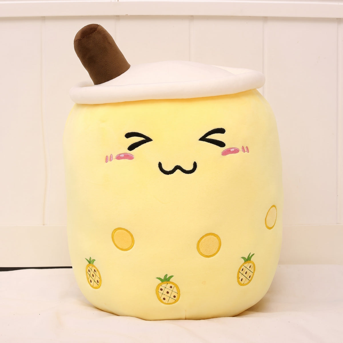 Boba Plush Pillow in yellow with pineapple prints, closed happy eyes and blushing cheeks, a plush bubble-tea cup with a cream lid, straw and pearls
