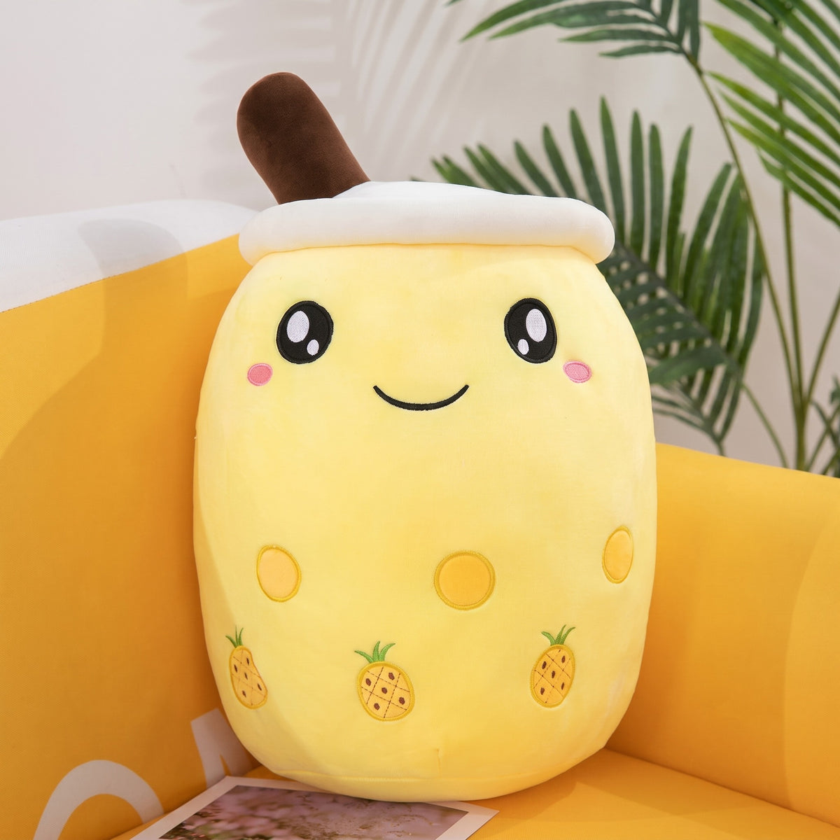 Boba Plush Pillow in yellow with pineapple prints, wide open eyes and blushing cheeks, a plush bubble-tea cup with a cream lid, straw and pearls