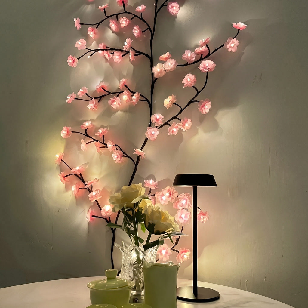 Pink Cherry Blossom Branch Light curving up a wall beside a table lamp and flowers