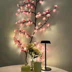 Pink Cherry Blossom Branch Light curving up a wall beside a table lamp and flowers