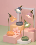 All four colorways of the Flower LED Desk Lamp - blue, pink, apricot, and green - lit, on pastel display blocks
