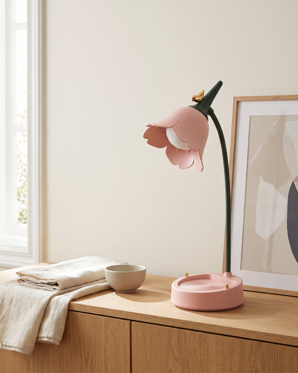 Flower LED Desk Lamp in pink, switched off, on an oak sideboard beside a framed print