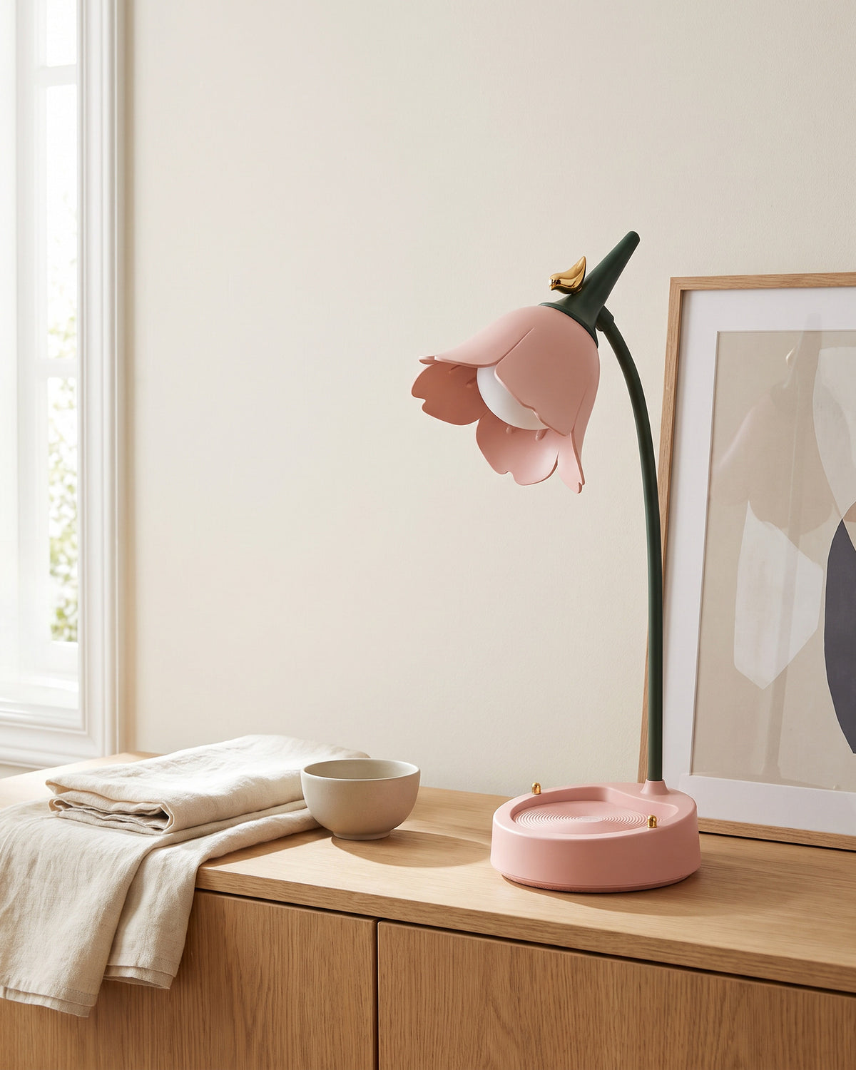 Flower LED Desk Lamp in pink, switched off, on an oak sideboard beside a framed print