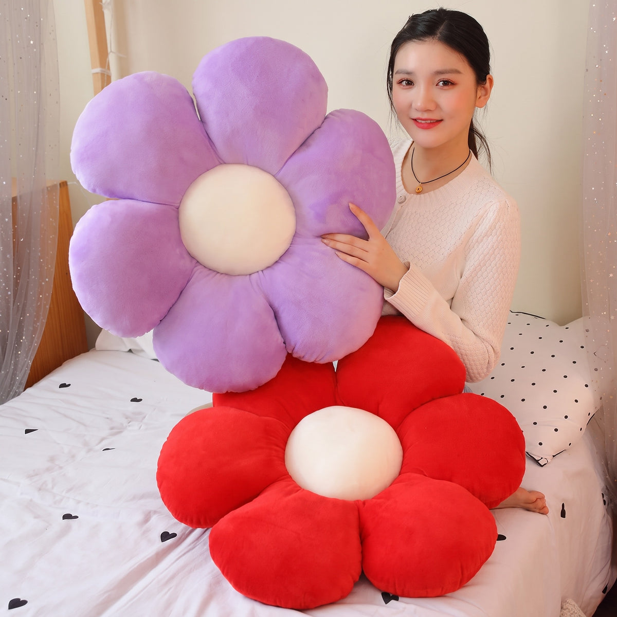 Model holding a purple Flower Plush Pillow, with a red one on the bed