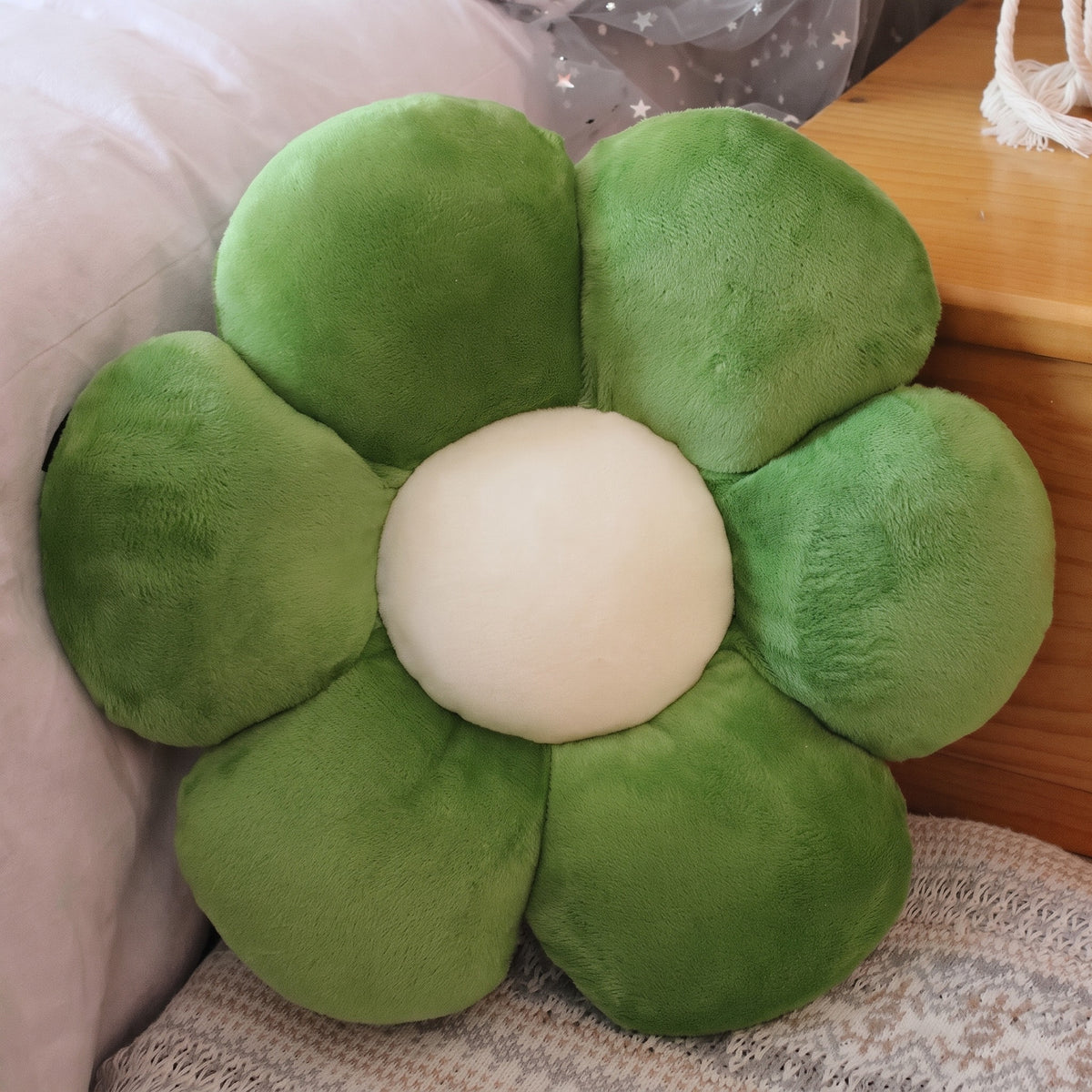 Flower Plush Pillow in dark green with a cream center, six plush petals, on a bed