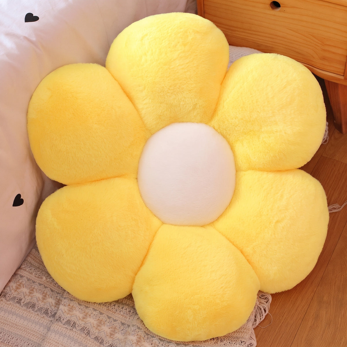Flower Plush Pillow in fluffy yellow with a cream center, six plush petals, on a bed