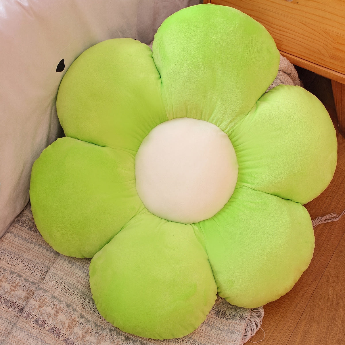 Flower Plush Pillow in light green with a cream center, six plush petals, on a bed