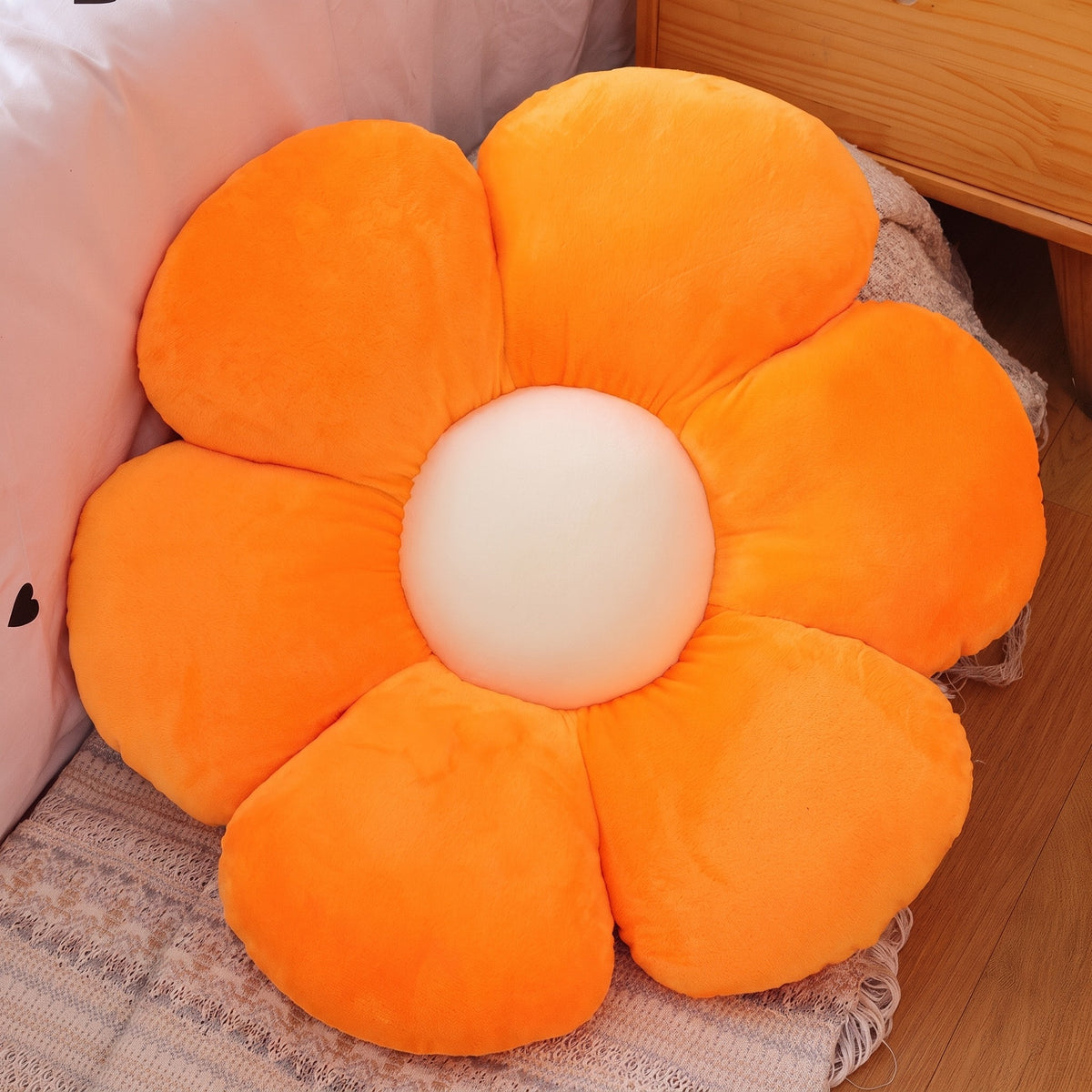 Flower Plush Pillow in orange with a cream center, six plush petals, on a bed