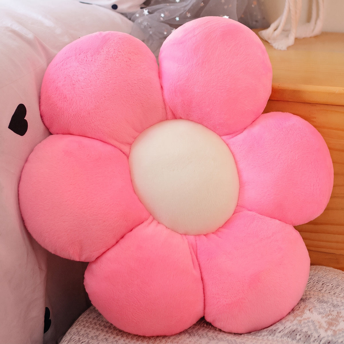 Flower Plush Pillow in pink with a cream center, six plush petals, on a bed