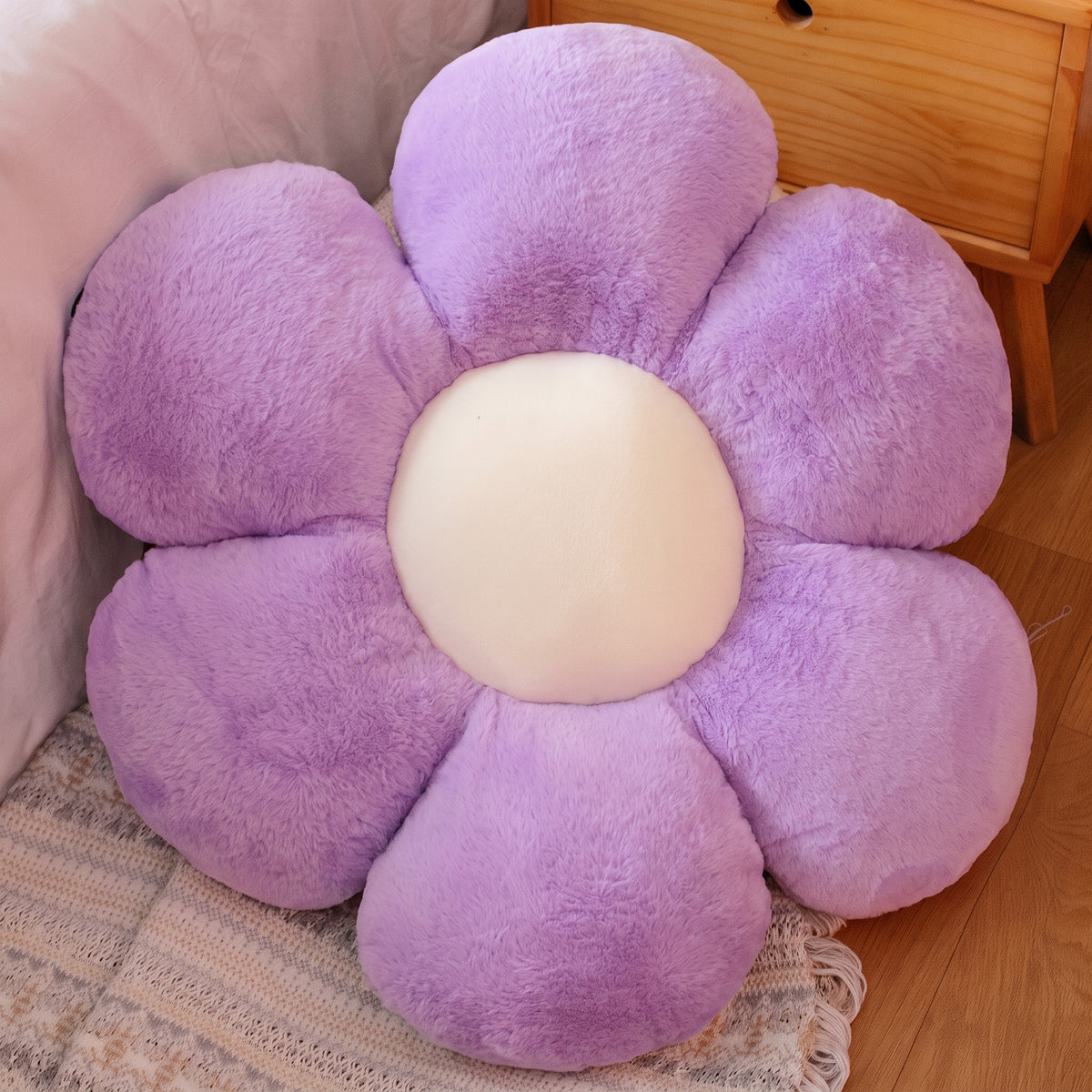 Flower Plush Pillow in purple with a cream center, six plush petals, on a bed