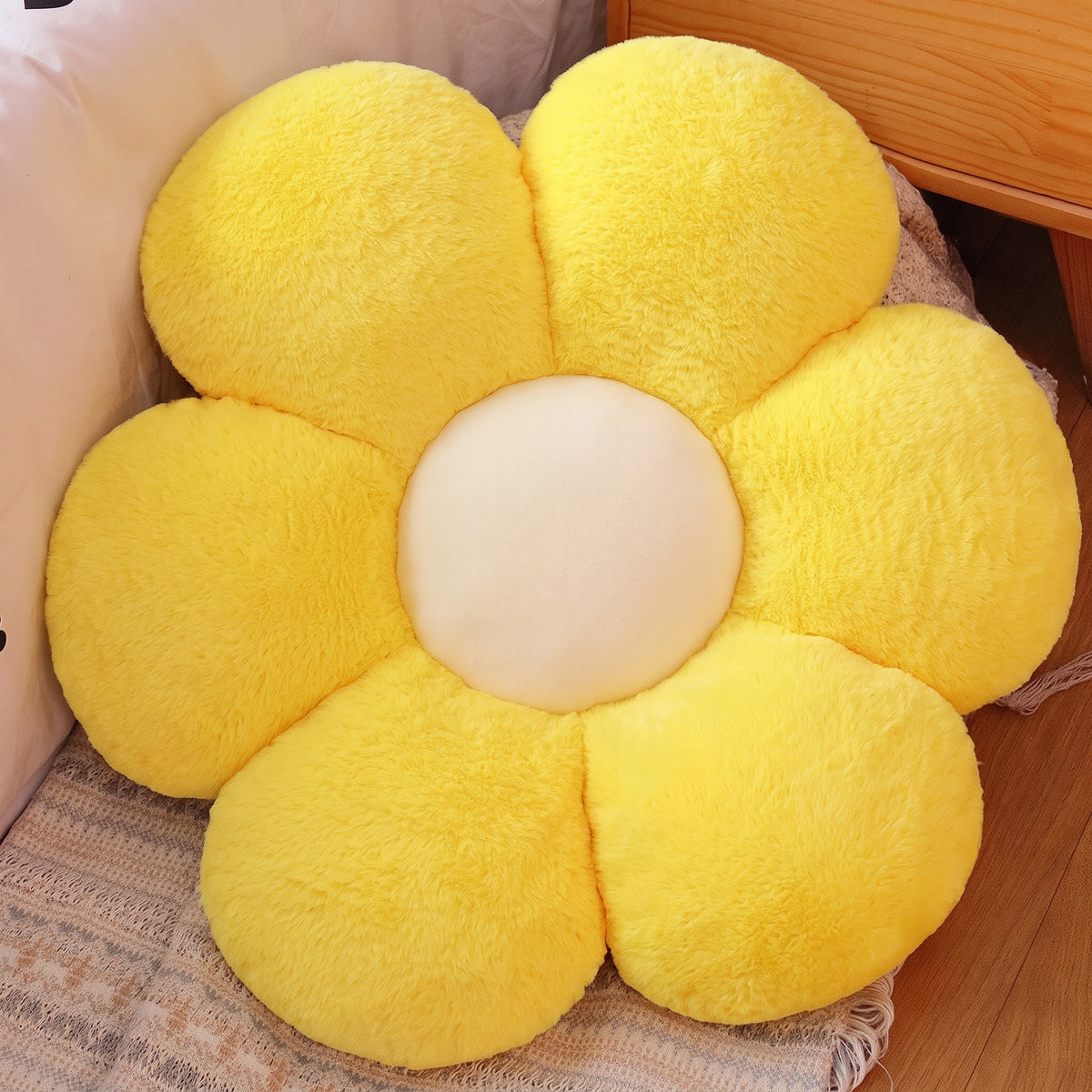 Flower Plush Pillow in yellow with a cream center, six plush petals, on a bed