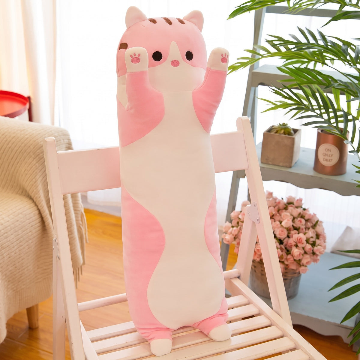 Long Cat Plush Pillow in pink, a slim plush cat with a white belly and raised paws, standing on a white chair