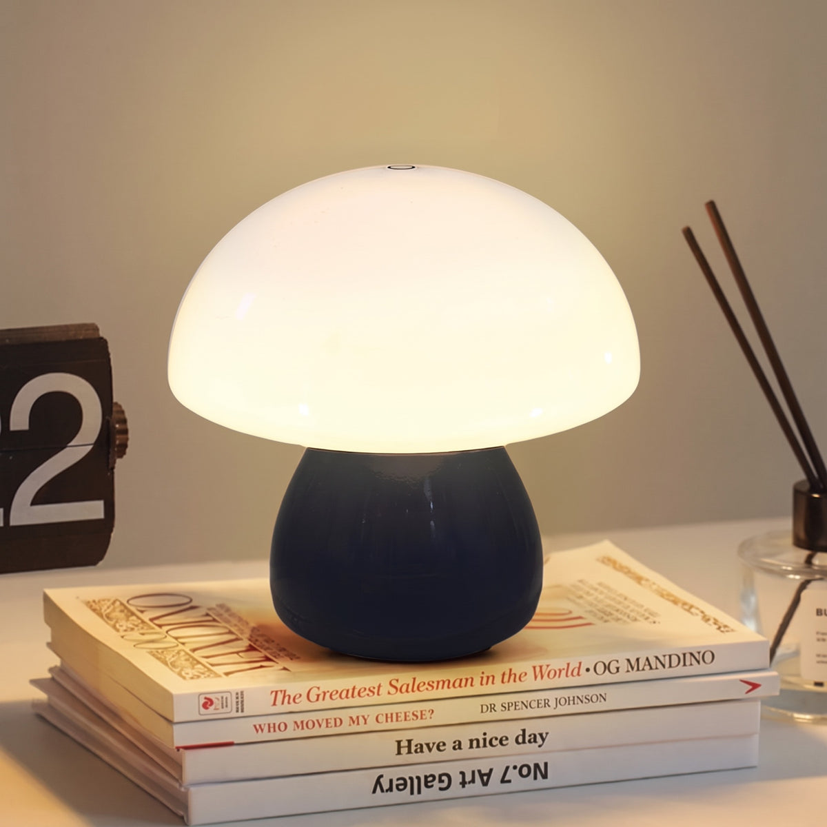Mini Mushroom Touch Lamp in Black lit warm on a stack of books beside a flip clock