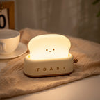 Toaster Night Light in cream, lit, on a linen cloth beside a coffee cup