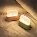 Toaster Night Lights in pink and mint, lit, on a bed
